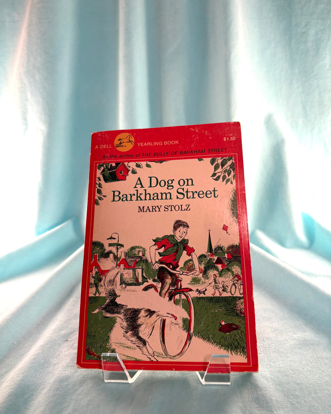 Book titled 'A Dog on Barkham Street' by Mary Stolz on a clear stand against a light blue curtain background.