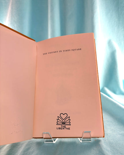 Open book with text 'The Cricket in Times Square' and logo on a light blue background