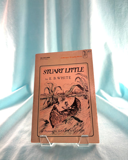Book cover of 'Stuart Little' by E.B. White on a stand against a light blue curtain background