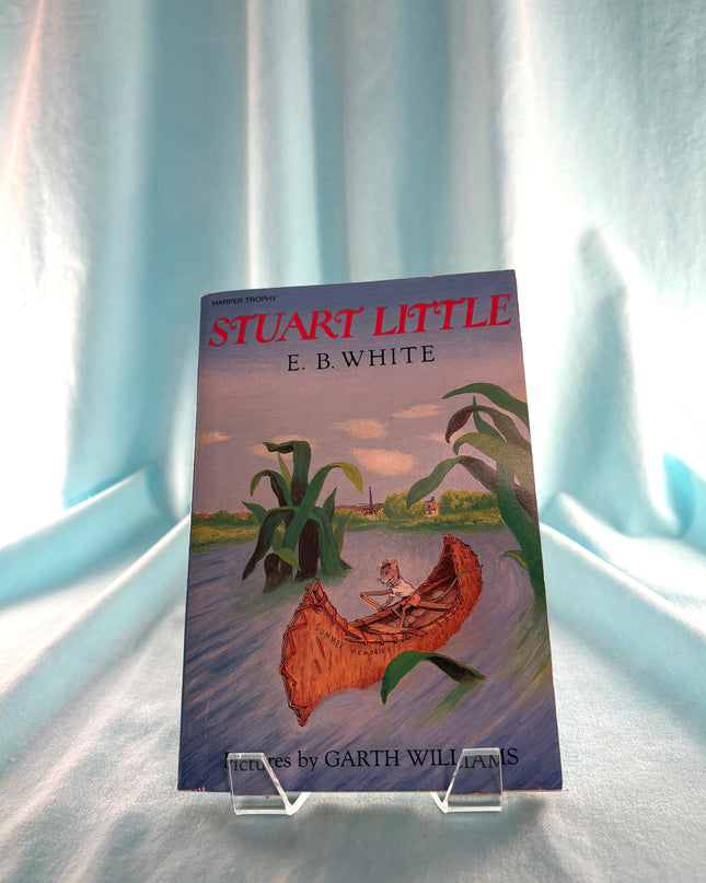 Book titled 'Stuart Little' by E.B. White on a clear stand against a light curtain background