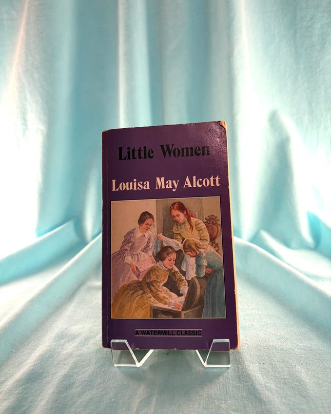 Book titled 'Little Women' by Louisa May Alcott on a light blue fabric background