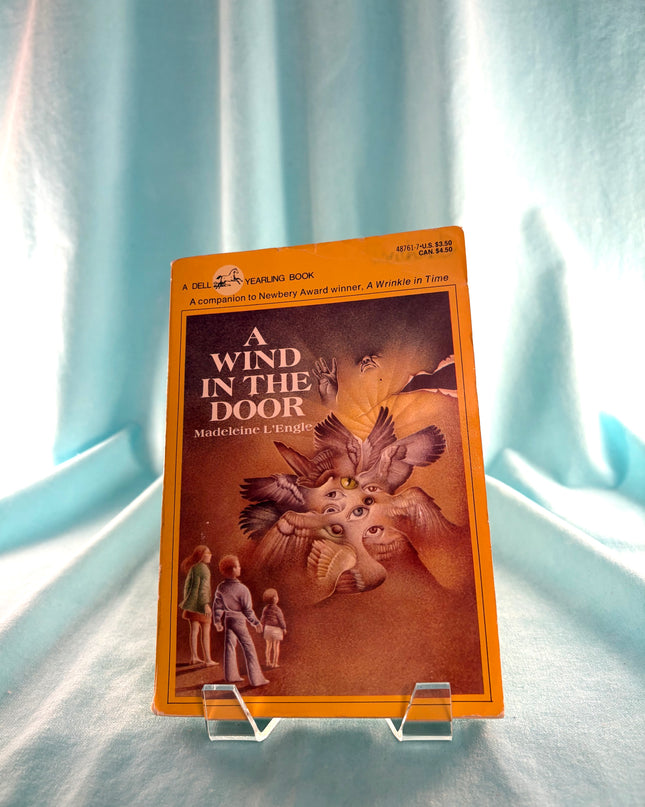Book titled 'A Wind in the Door' on a stand with a light blue curtain background