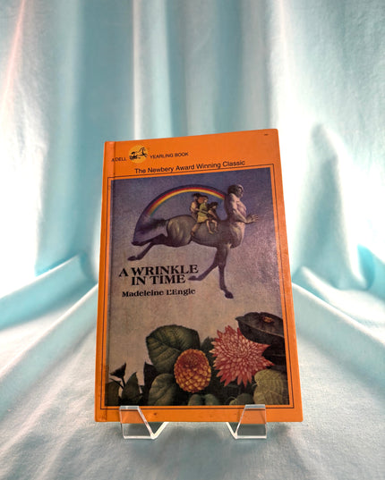 Book titled 'A Wrinkle in Time' by Madeleine L'Engle on a stand against a light blue curtain background
