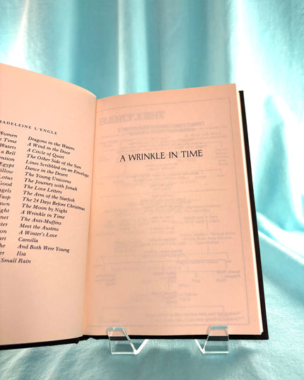 Open book titled 'A Wrinkle in Time' on a clear stand with a light blue curtain background