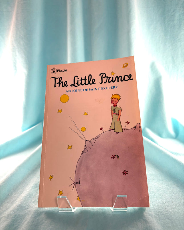 Book titled 'The Little Prince' on a stand with a light blue curtain background