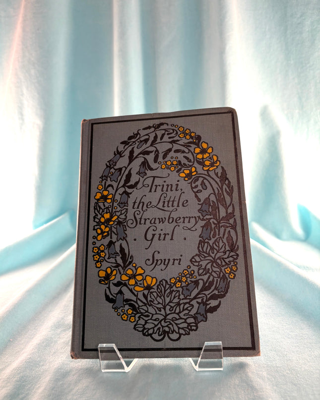 Book titled 'Trini, the Little Strawberry Girl' by Spyri on a stand against a light curtain background