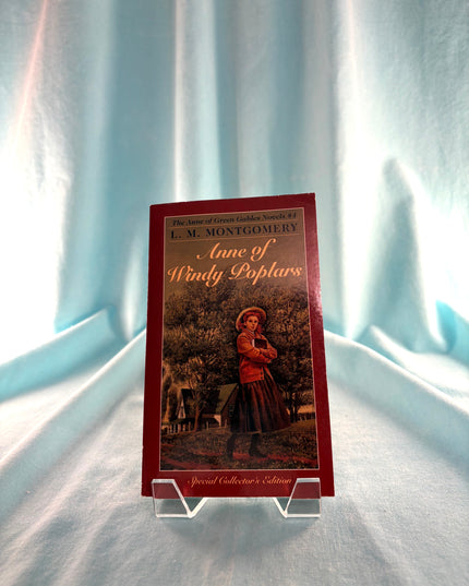 Book titled 'Anne of Windy Poplars' by L.M. Montgomery on a stand against a light curtain background