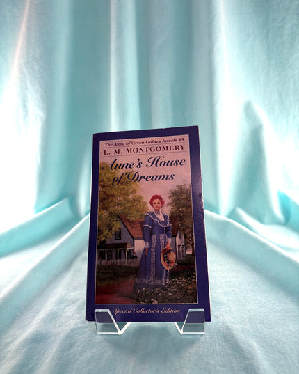 Book titled 'Anne's House of Dreams' by L.M. Montgomery on a stand against a light blue curtain background