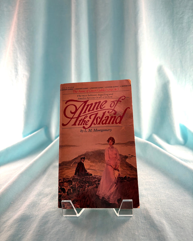 Book titled 'Anne of the Island' by L.M. Montgomery on a stand against a light curtain background