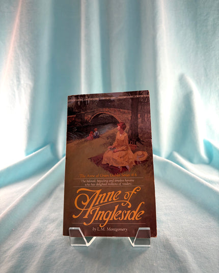 Book titled 'Anne of Ingleside' on a stand with a light blue curtain background