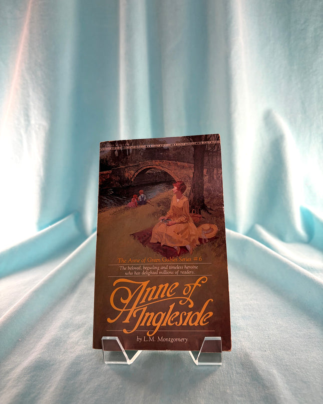 Book titled 'Anne of Ingleside' on a stand with a light blue curtain background