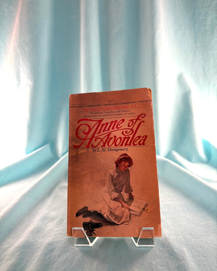 Book titled 'Anne of Avonlea' on a stand with a light blue curtain background