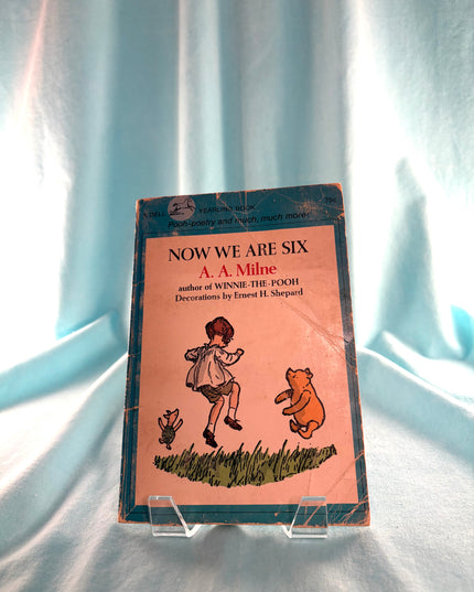 Book titled 'Now We Are Six' by A. A. Milne on a light blue fabric background