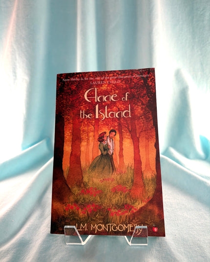 Book cover of 'Anne of the Island' by L.M. Montgomery on a stand against a light blue curtain background