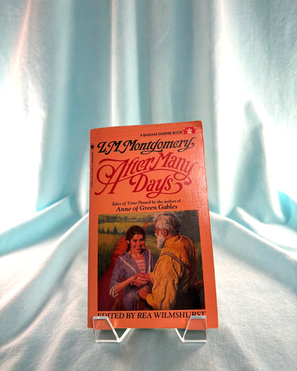 Book titled 'After Many Days' by L.M. Montgomery on a stand against a light blue curtain background