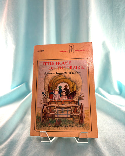 Book titled 'Little House on the Prairie' by Laura Ingalls Wilder on a light blue fabric background