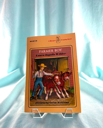 Book cover of 'Farmer Boy' by Laura Ingalls Wilder on a light blue fabric background
