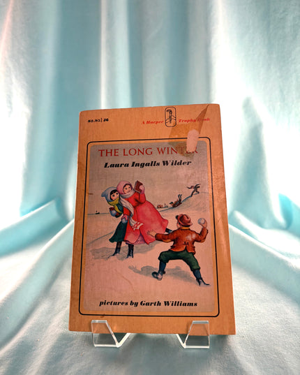 Book cover of 'The Long Winter' by Laura Ingalls Wilder on a light blue fabric background