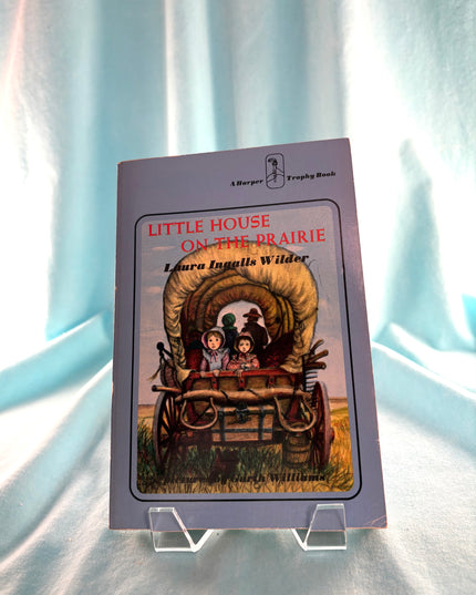 Book titled 'Little House on the Prairie' by Laura Ingalls Wilder on a light blue fabric background