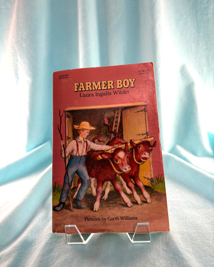 Book titled 'Farmer Boy' by Laura Ingalls Wilder on a light blue fabric background