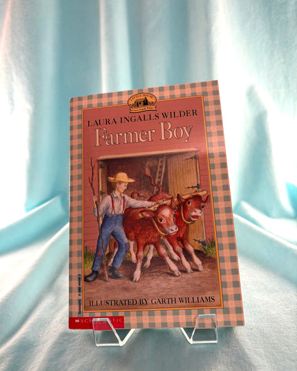 Book titled 'Farmer Boy' by Laura Ingalls Wilder on a light blue background