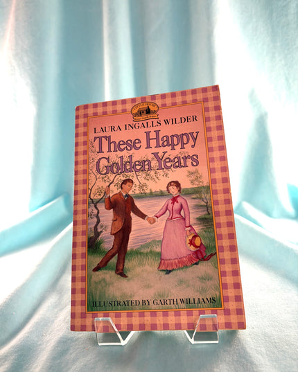 Book titled 'These Happy Golden Years' by Laura Ingalls Wilder on a light blue fabric background