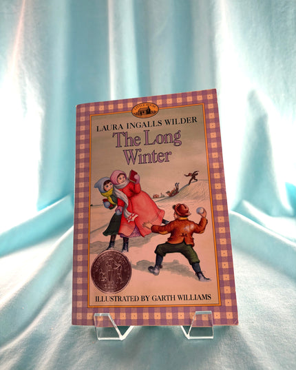 Book titled 'The Long Winter' by Laura Ingalls Wilder on a stand with a checkered border.