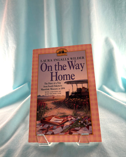 Book titled 'On the Way Home' by Laura Ingalls Wilder on a stand against a light background