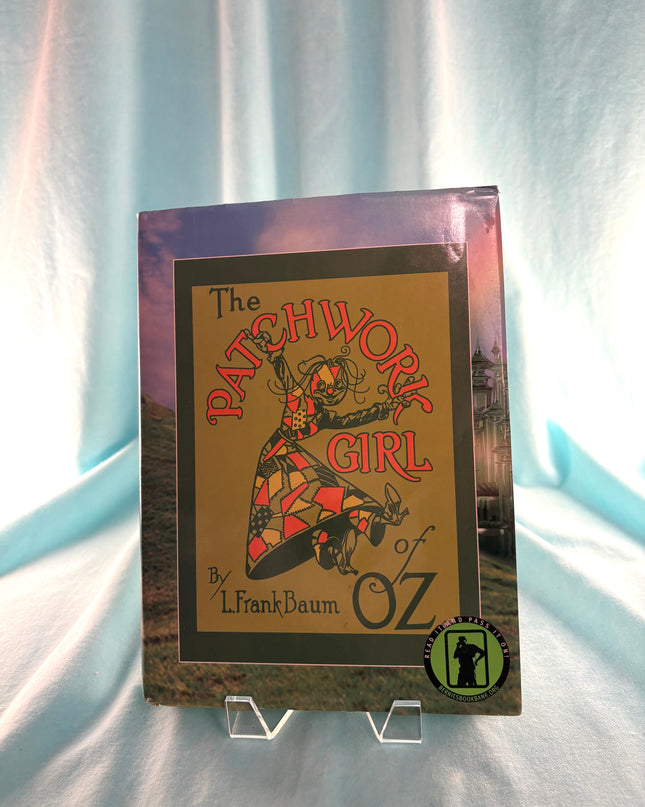 Book titled 'The Patchwork Girl of Oz' by L. Frank Baum on a stand with a light blue curtain background