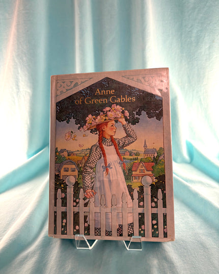 Book titled 'Anne of Green Gables' on a stand against a light blue curtain background