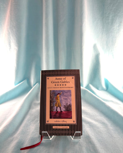 Book titled 'Anne of Green Gables' by L.M. Montgomery on a stand against a light curtain background