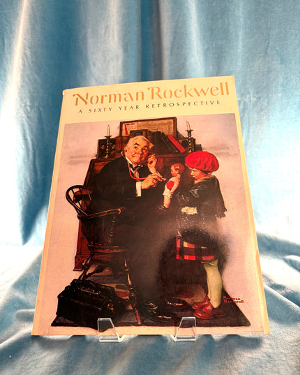 Booklet titled 'Norman Rockwell: A Sixty-Year Retrospective' on a textured blue background