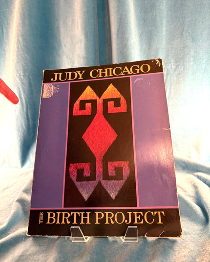 Book titled 'The Birth Project' by Judy Chicago on a light blue fabric background