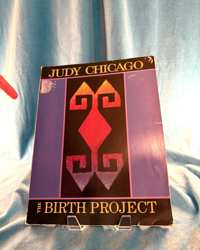 Book titled 'The Birth Project' by Judy Chicago on a light blue fabric background