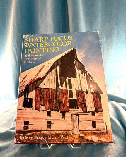 Book titled 'Sharp Focus Watercolor Painting' on a textured fabric background