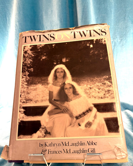 Book titled 'Twins on Twins' with a black and white photo of two women on the cover, placed on a blue fabric background. By Kathryn McLaughlin Abbe & Frances McLaughlin Gill