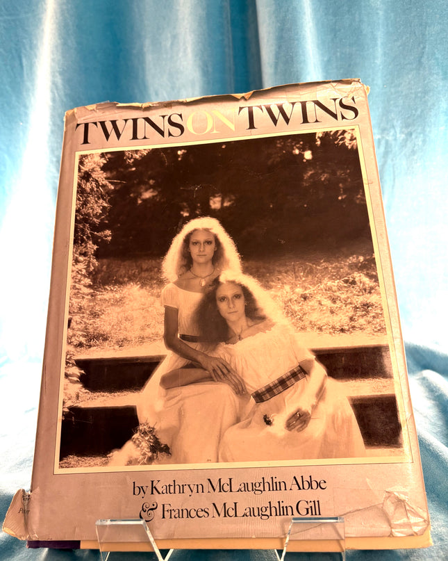 Book titled 'Twins on Twins' with a black and white photo of two women on the cover, placed on a blue fabric background. By Kathryn McLaughlin Abbe & Frances McLaughlin Gill