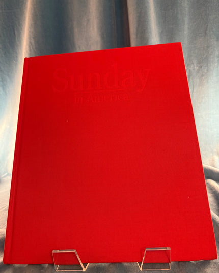 Red book titled 'Sunday in America' on a stand against a gray background