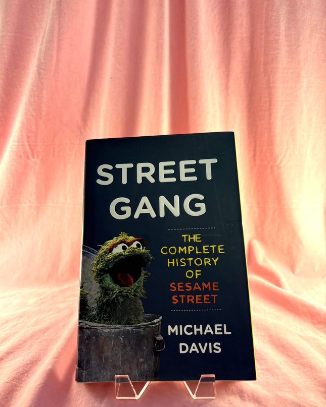 Book titled 'Street Gang: The Complete History of Sesame Street' by Michael Davis on a pink background